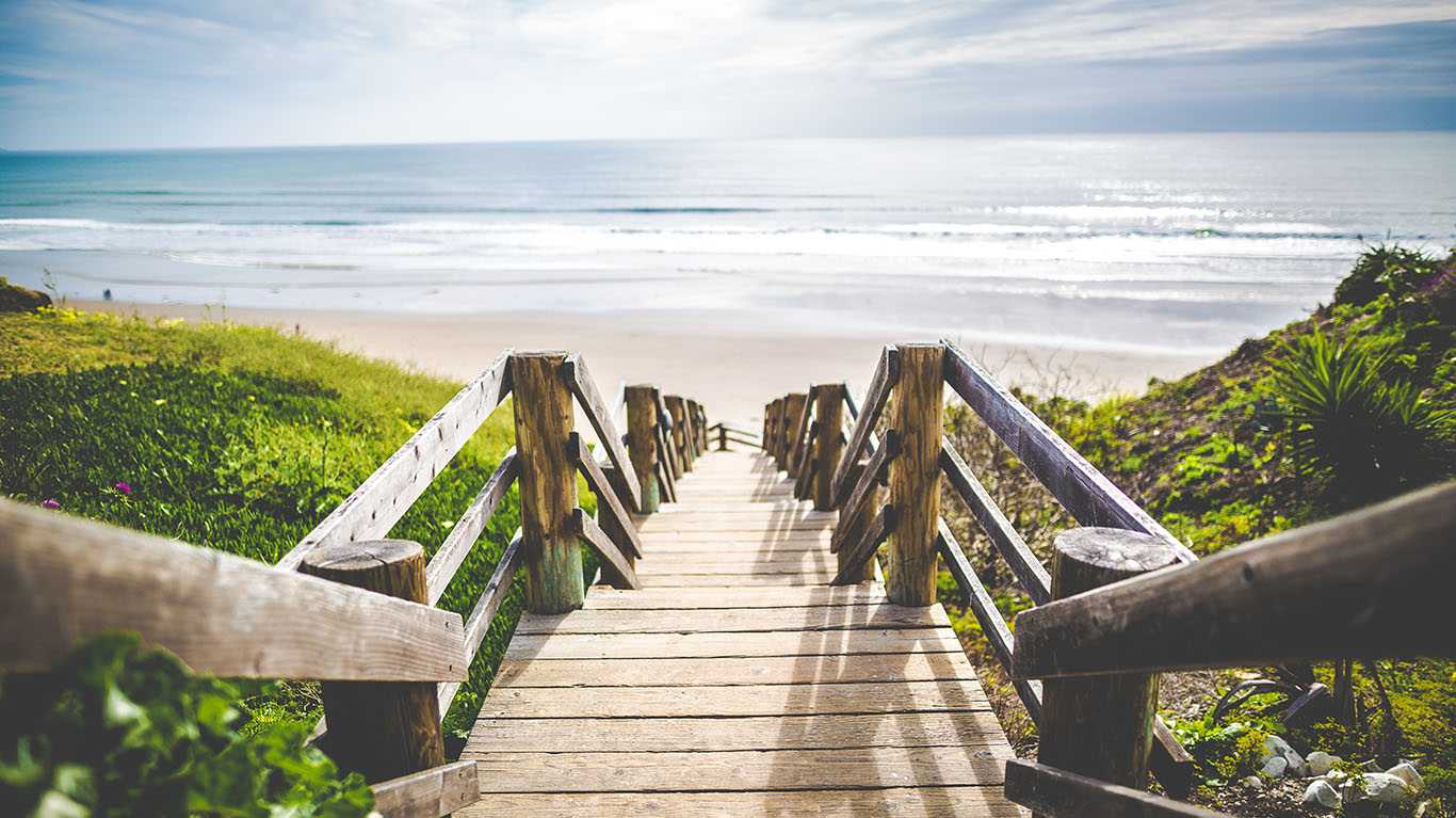 Uma escada de madeira no meio da vegetação leva até a praia.